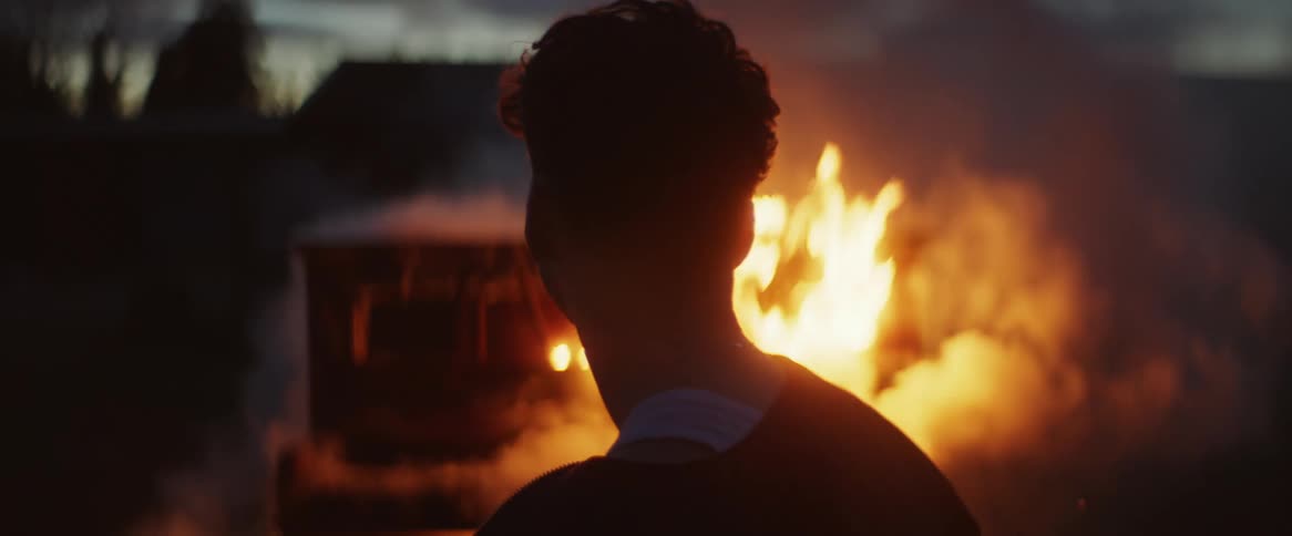 Man watches bonfire at dusk
