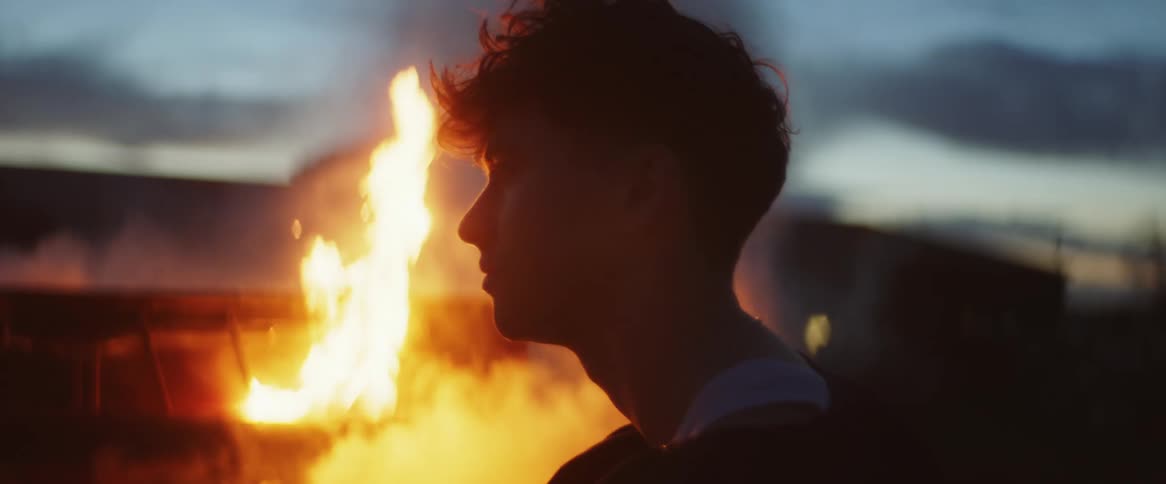 A males silhouette sitting in front of a bonfire at dusk