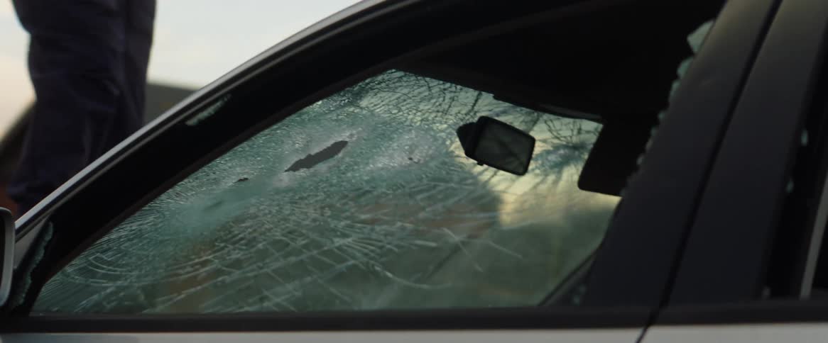 Person stands on hood of car swinging sledgehammer to shatter windshield