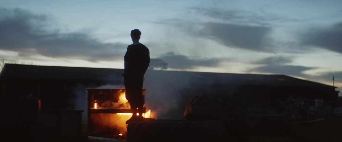 A man stands on top of a burning structure and watches the flames