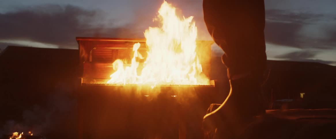 Man stands outdoors at night looking down at piano burning in field