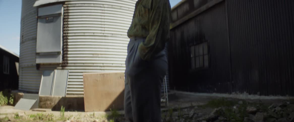 Man walks past corrugate metal silo outdoors during the day