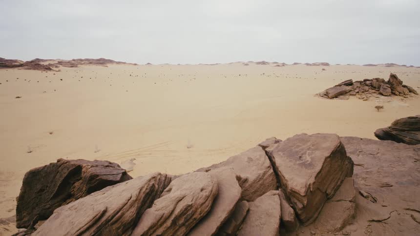 Piles of rocks and rock formations dot sand in desert under an overcast sky in Saudi Arabia