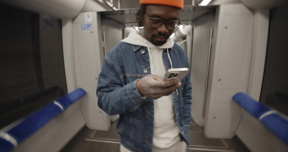 Young black man in casual attire texting on smartphone while riding in subway car