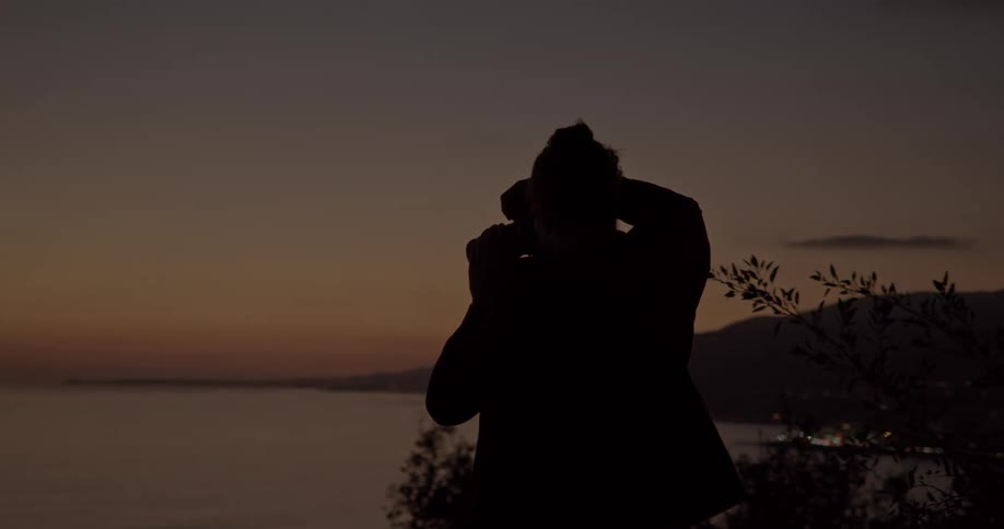 A man stands on a cliff overlooking the ocean