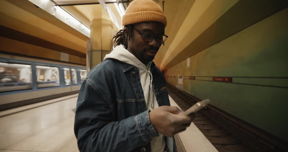 A man in a train station scrolls on his cell phone