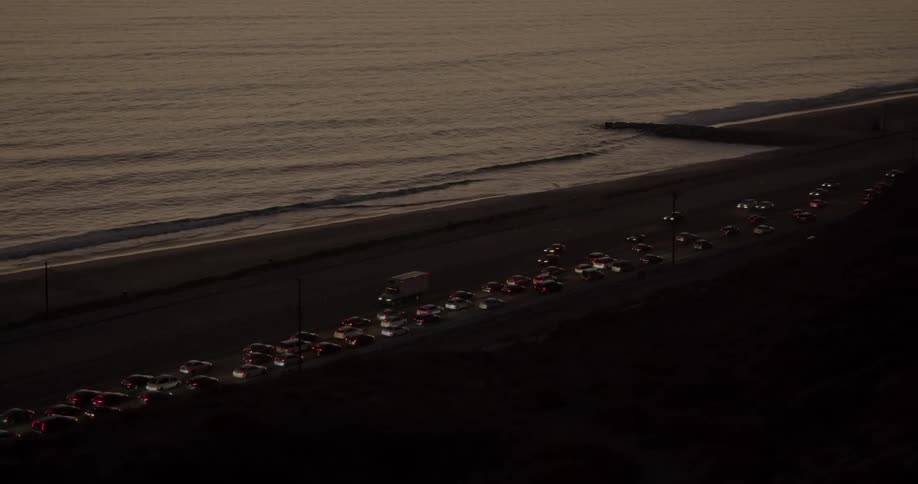 Traffic on one side of beach side highway flows smoothly at night while the other heavily crowded side flows slowly