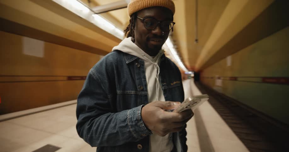A man uses his smartphone while standing on a platform in a subway station