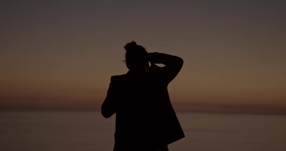 A woman stands on the shore and looks out at the ocean