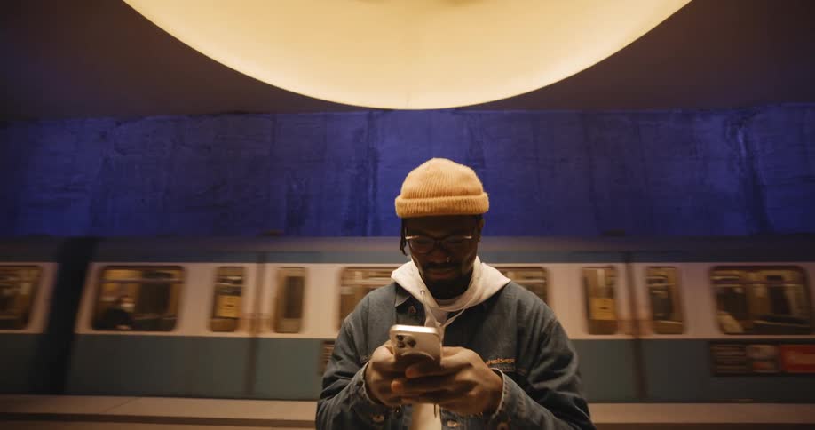Man scrolls on smartphone as subway train passes in the background