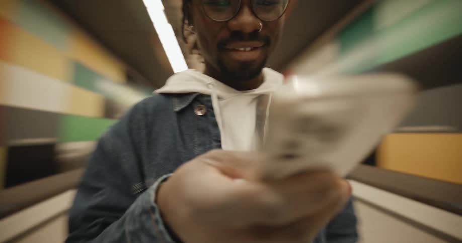 A man wearing a jacket and a knit cap is standing in a subway station texting on his phone