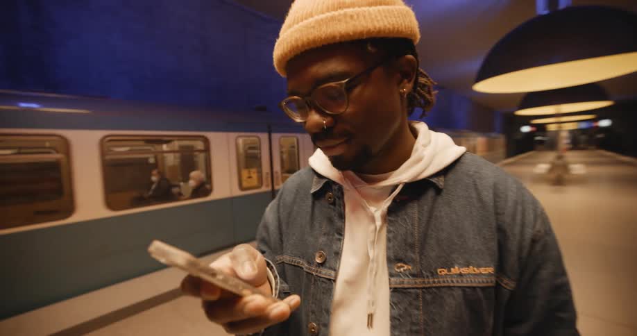 A man holding his cell phone stands next to a subway on the platform