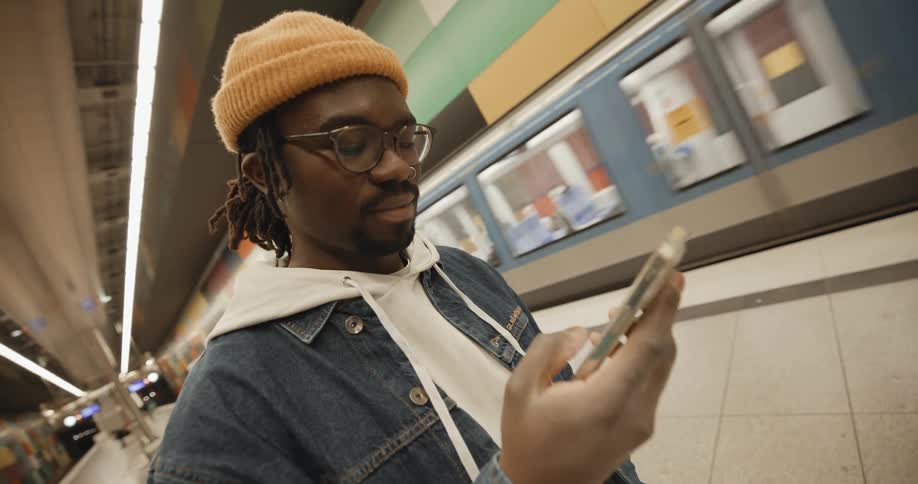 Man standing in station as train passes checks his smartphone