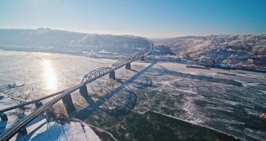 A river is frozen over under a bridge connected to a mountain range