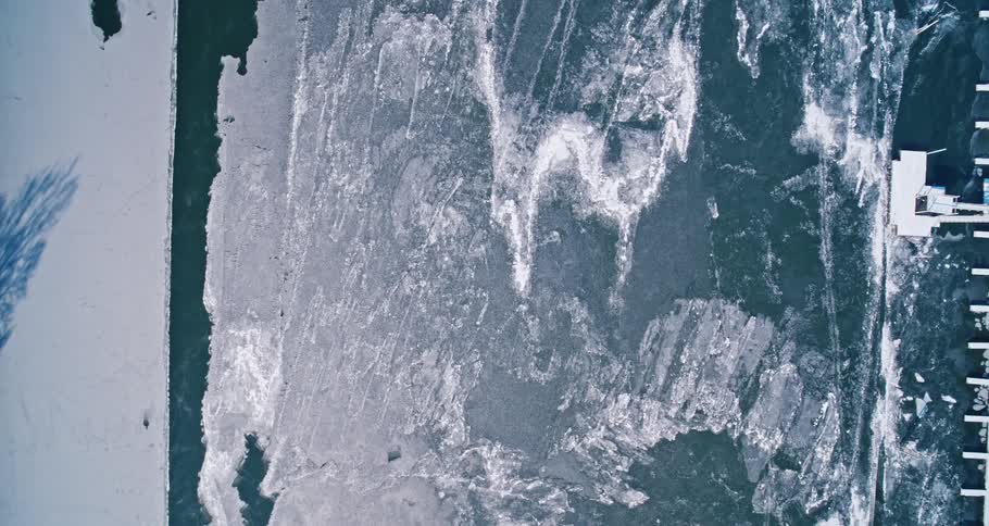 A frozen river with empty docks as the ice is cracked and water is moving near the shore