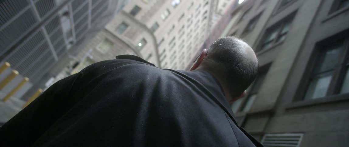 A man stands in the middle of the street looking up at the high rises around him
