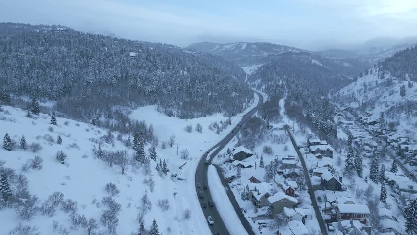 An aerial over a snow covered mountain town with a few houses and a road with traffic traveling it