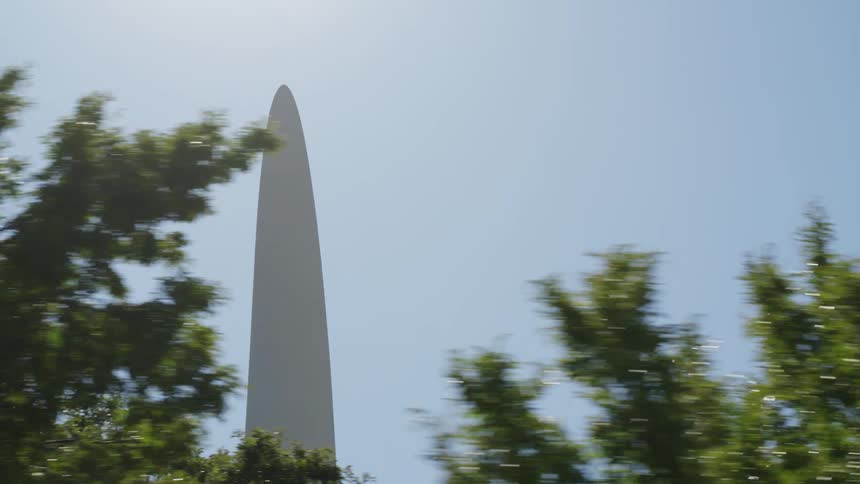 Sun shines onto trees and obelisk under a clear sky