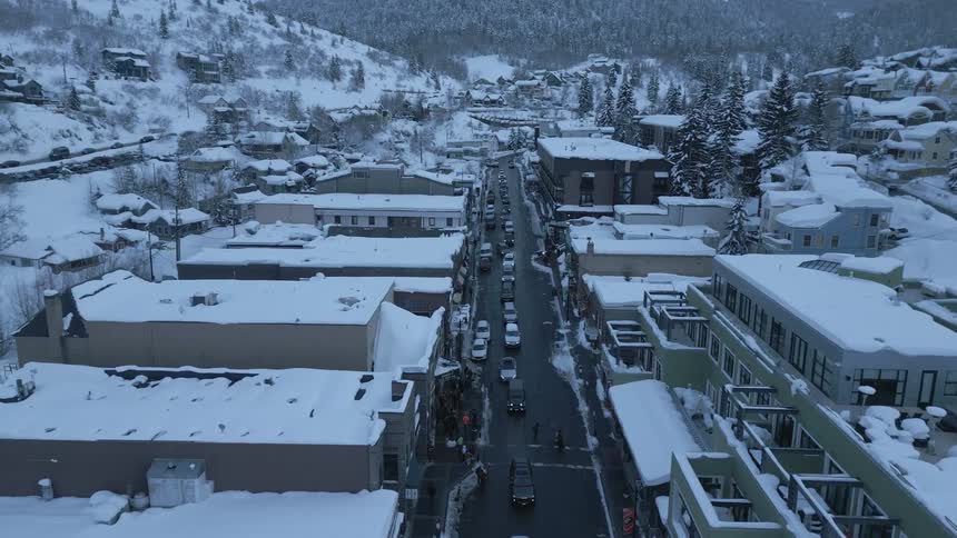 Line of vehicles drives along road separating snow covered buildings in valley