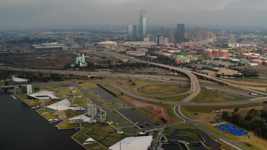 Traffic flows along highway between amusement park on the water on one side and foggy city downtown on the other