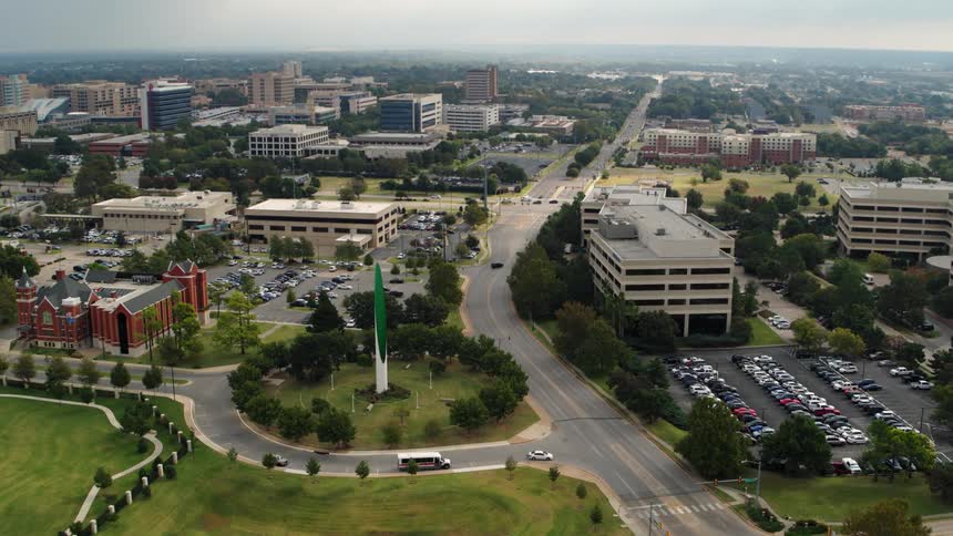 Aerial view of a roundabout with a monument in the middle of it surrounded by trees and grass in a city
