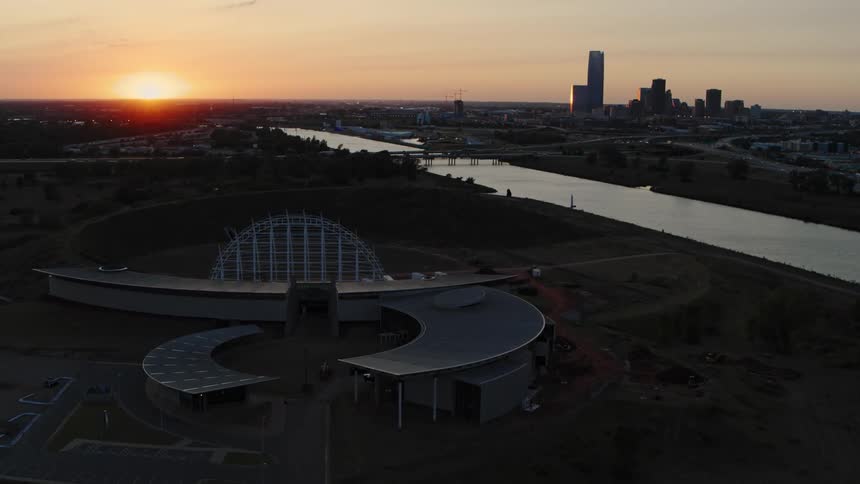 A sun setting over a city skyline and an arena event center in the foreground