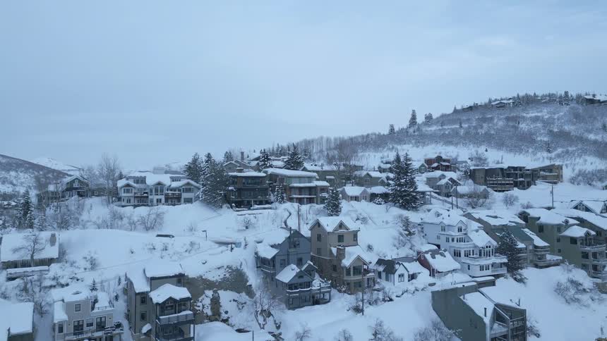 An aerial view of cars and snow plows driving past snow covered houses in a neighborhood