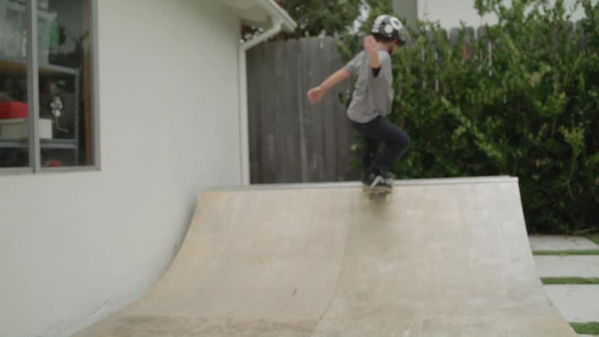 A boy riding his skateboard on a ramp in his back yard