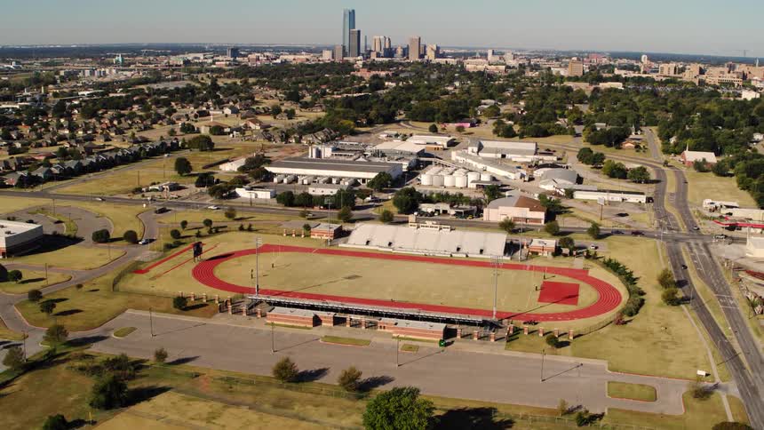 Cars drive past running track and stands on the way to the skyline on the horizon