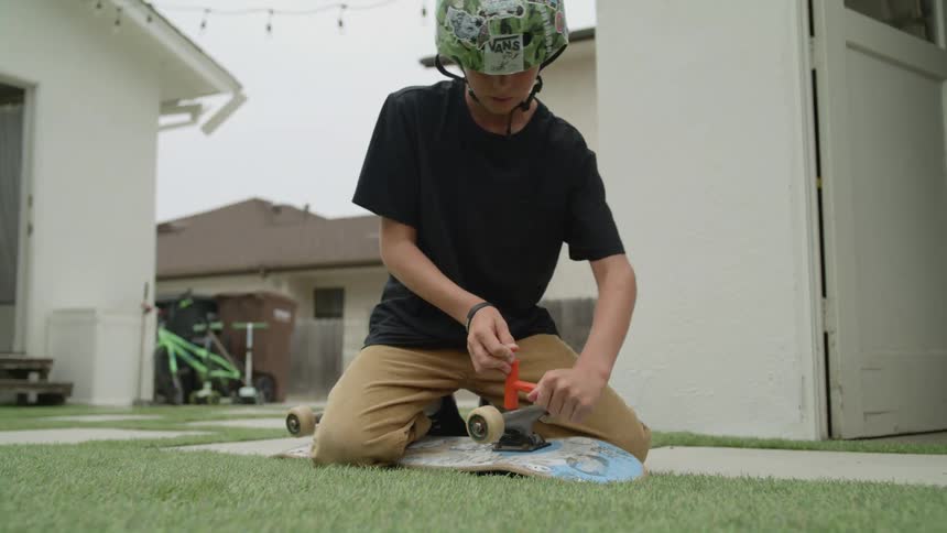 Youth kneels on lawnin backyard attaching wheels to skateboard