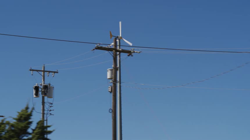 A tall windmill off in the distance behind trees and poles