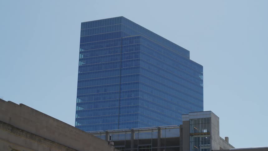 Blocky blue building towers over mid and low rise buildings under a slightly cloudy sky