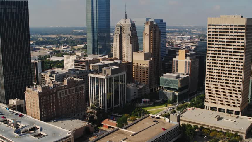 The sun shines upon tall buildings and skyscrapers in a metropolitan city as traffic moves on the street