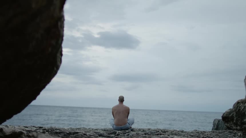 A man sitting cross legged on the beach looking out onto the ocean