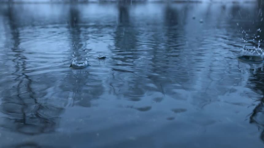 A up close of water dripping and creating ripples on the water on the ground