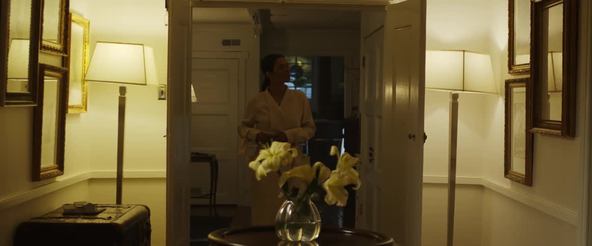 A woman is walking into a room and smelling flowers