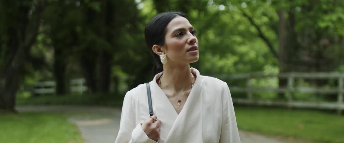 An elegant woman walks on a gravel road through a park admiring the view