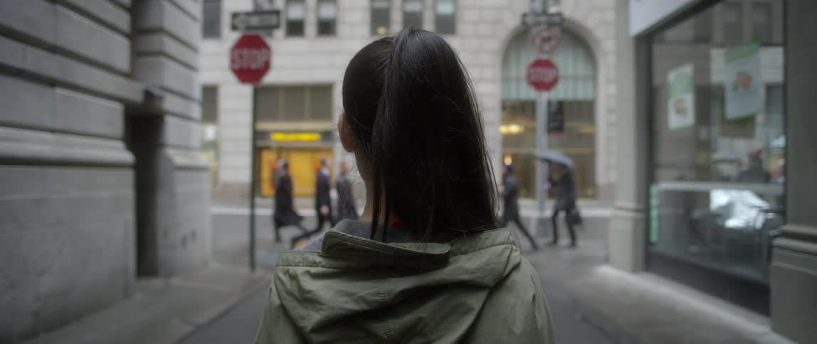 Woman standing in alley facing towards a pedestrian busy city street
