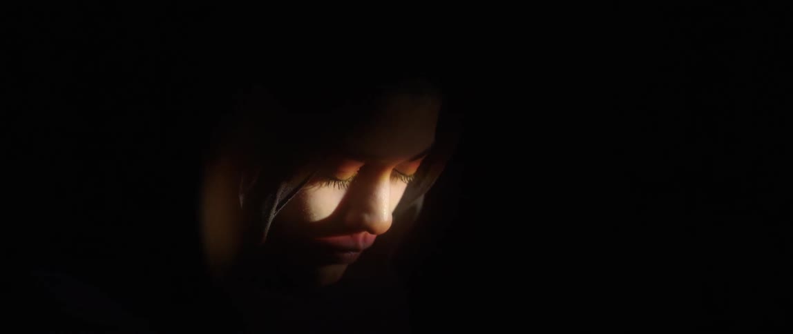 A woman is in the dark with only a little light on her face