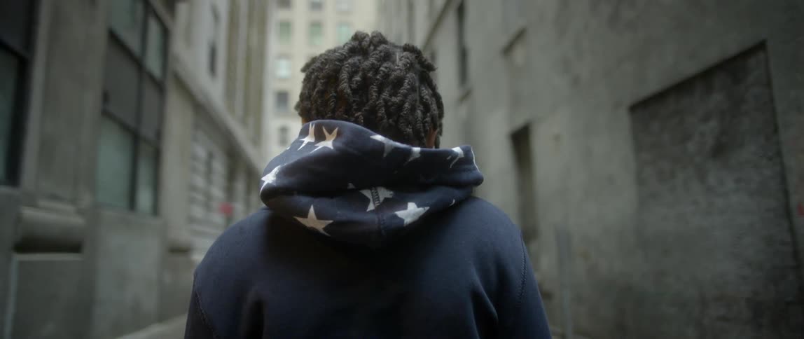 A man removes his hood in an alley