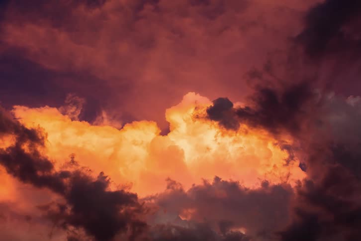 Sunset colored clouds move across a surreal sky as bright illuminated clouds move in the other direction in the distance as the purple and pink become blue