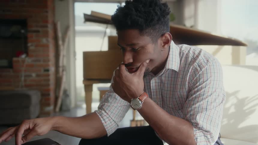 A man is sitting at a table with one hand on his face and typing on a computer with the other hand