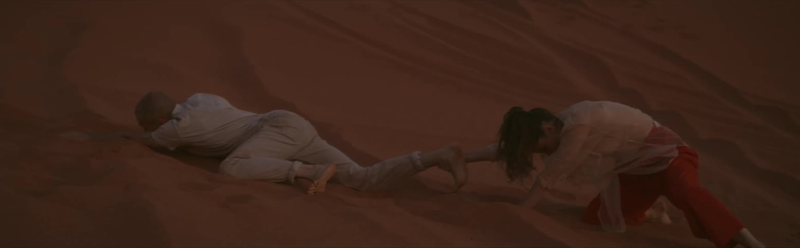 A woman dragging a man in the sand as he flops around