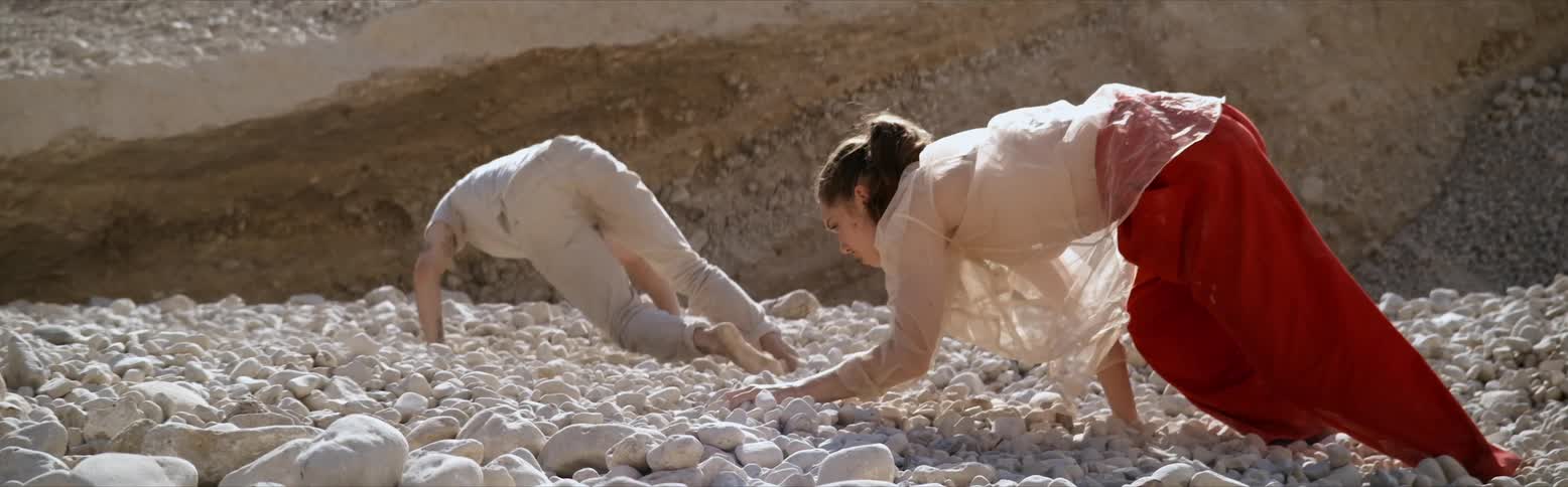 Two people crawl across white rocks on their hands and feet during the day