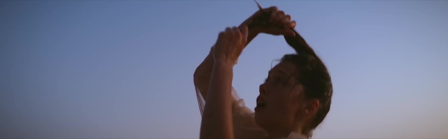 Woman in sheer blouse and red pants pulling her ponytail and doing unusual modern dance movements in the desert