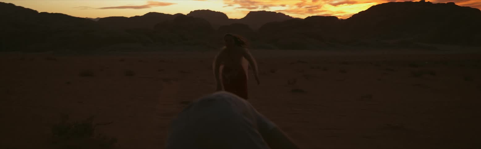 Two people running and falling in the desert while the sun sets