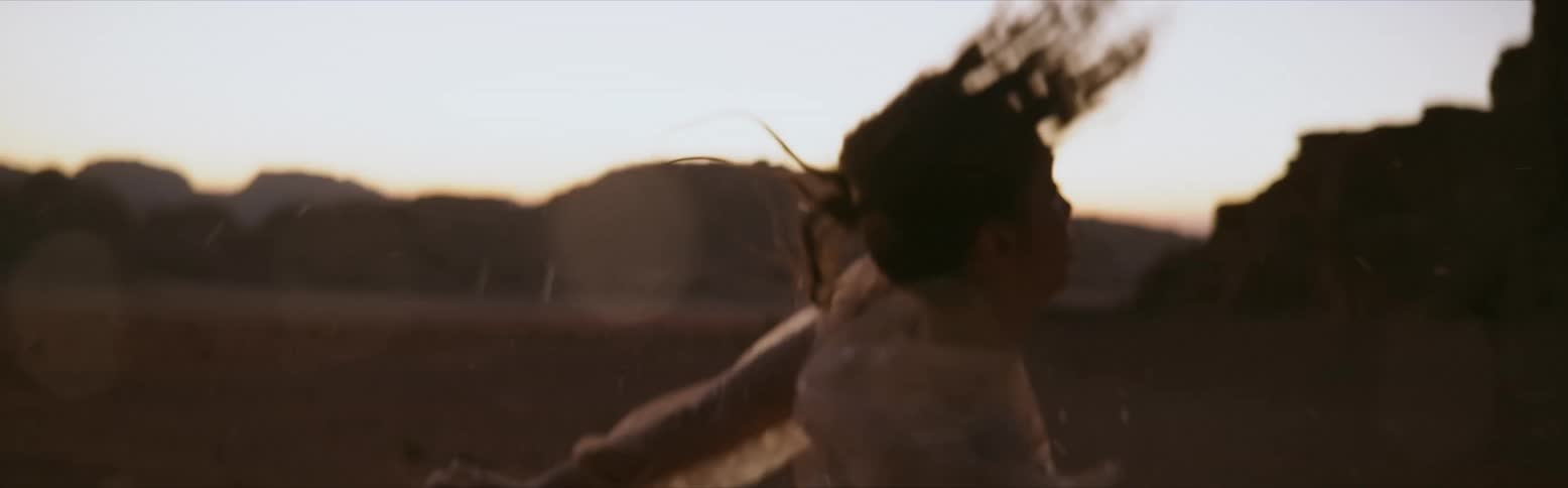 A woman is dancing wildly in the desert spinning and raising her arms in the air