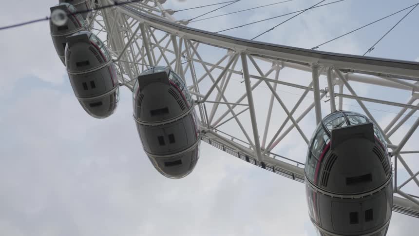 Egg shaped cars on white ferris wheel contrast with cloudy sky