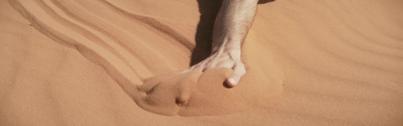 Shavedhead man falls to ground crawls on sand drags hand across sand in desert