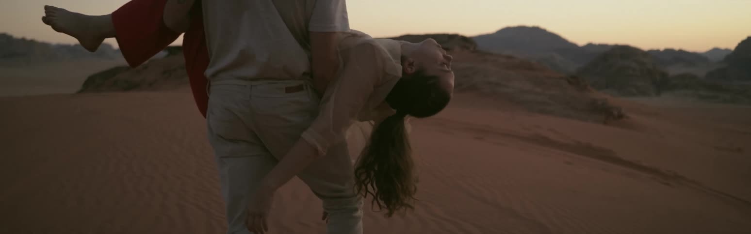 A man is carrying an unconscious woman in his arms across the desert